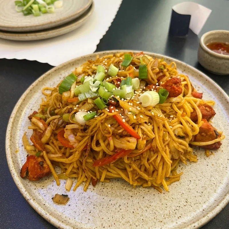 Chowmein plated at the table, the dining room behind it
